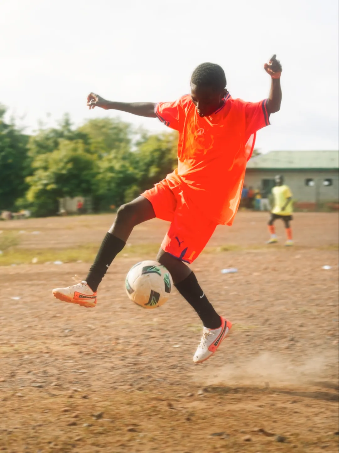 A boy kicking a soccer ball on a dirt pitch